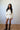 Woman wearing a white outfit with long sleeves and shorts, standing against a plain wall.